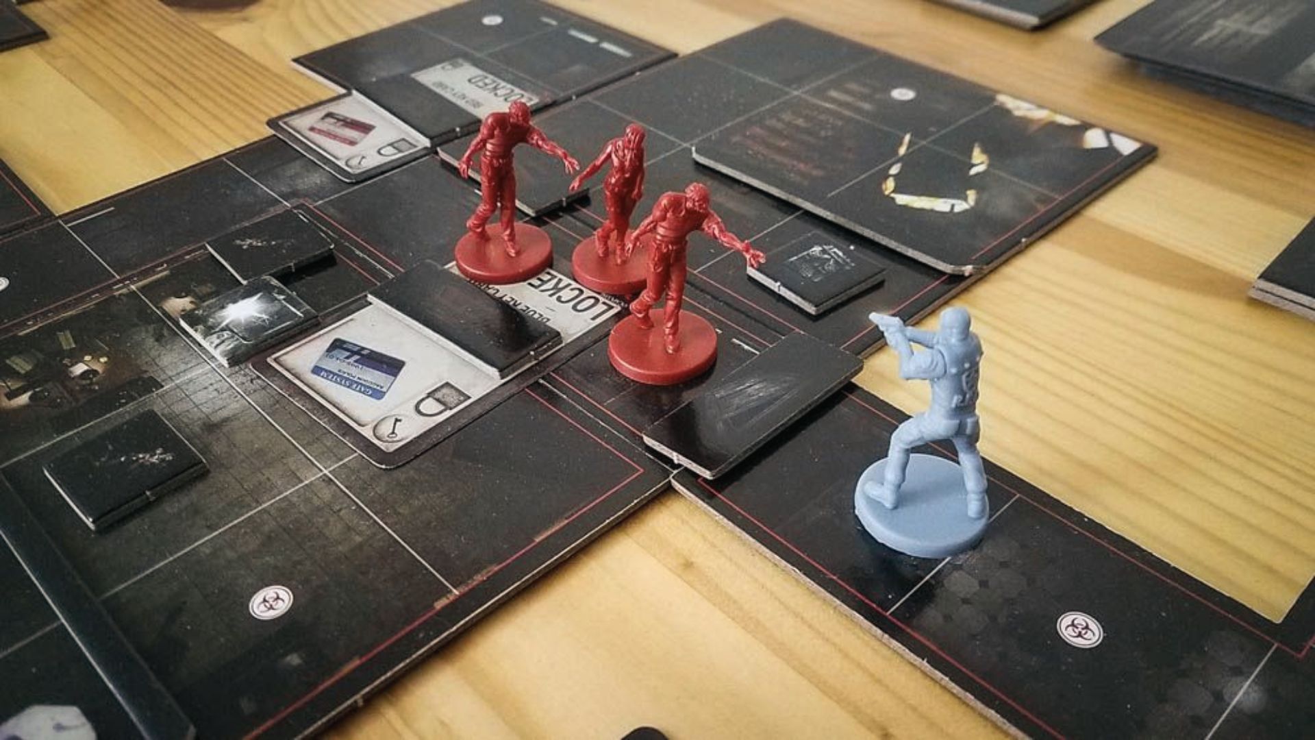 Lone survivor mini aims at three approaching zombies near locked doors on grim RPD map tiles.