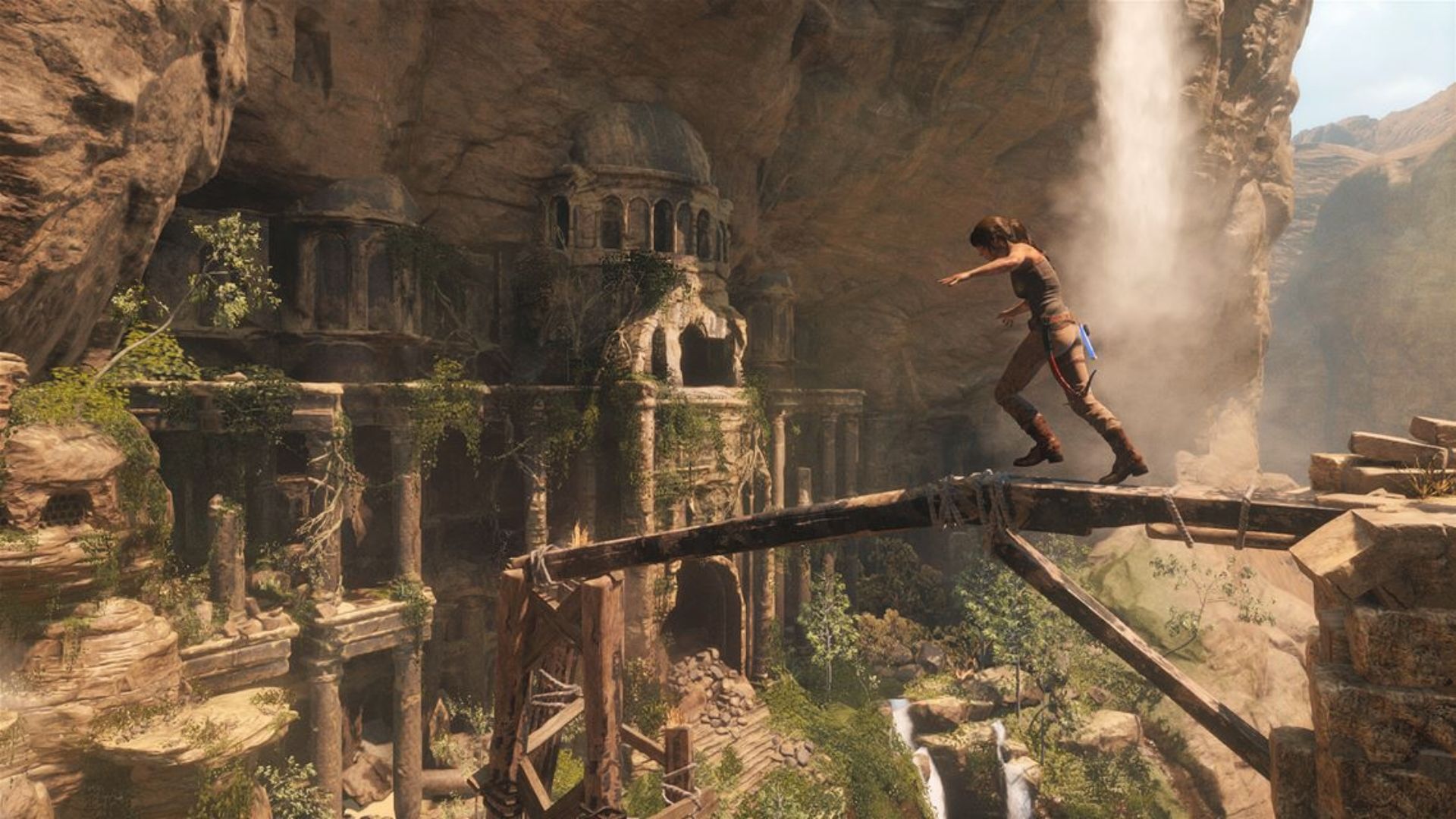 Lara balances on a beam above waterfall ruins. Rise of the Tomb Raider delivers tense platforming moments.