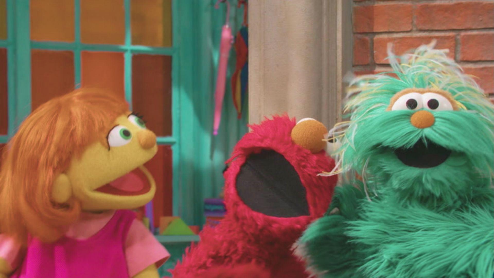 Red furry muppet Elmo from Sesame Street laughs with his mouth wide open between two other puppets.