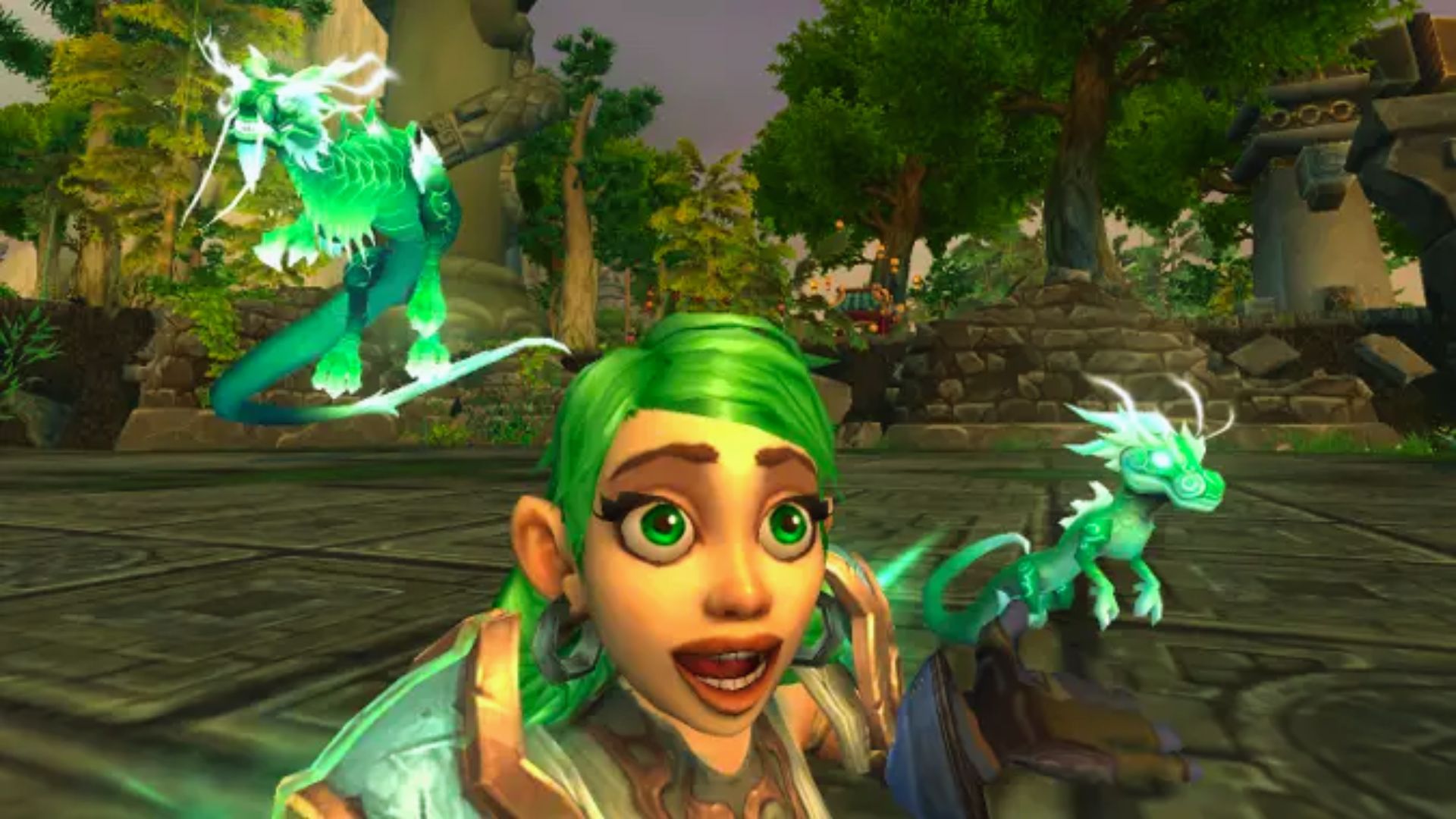 "World of Warcraft selfie of a smiling green-haired gnome with two glowing green dragon pets behind her.”
