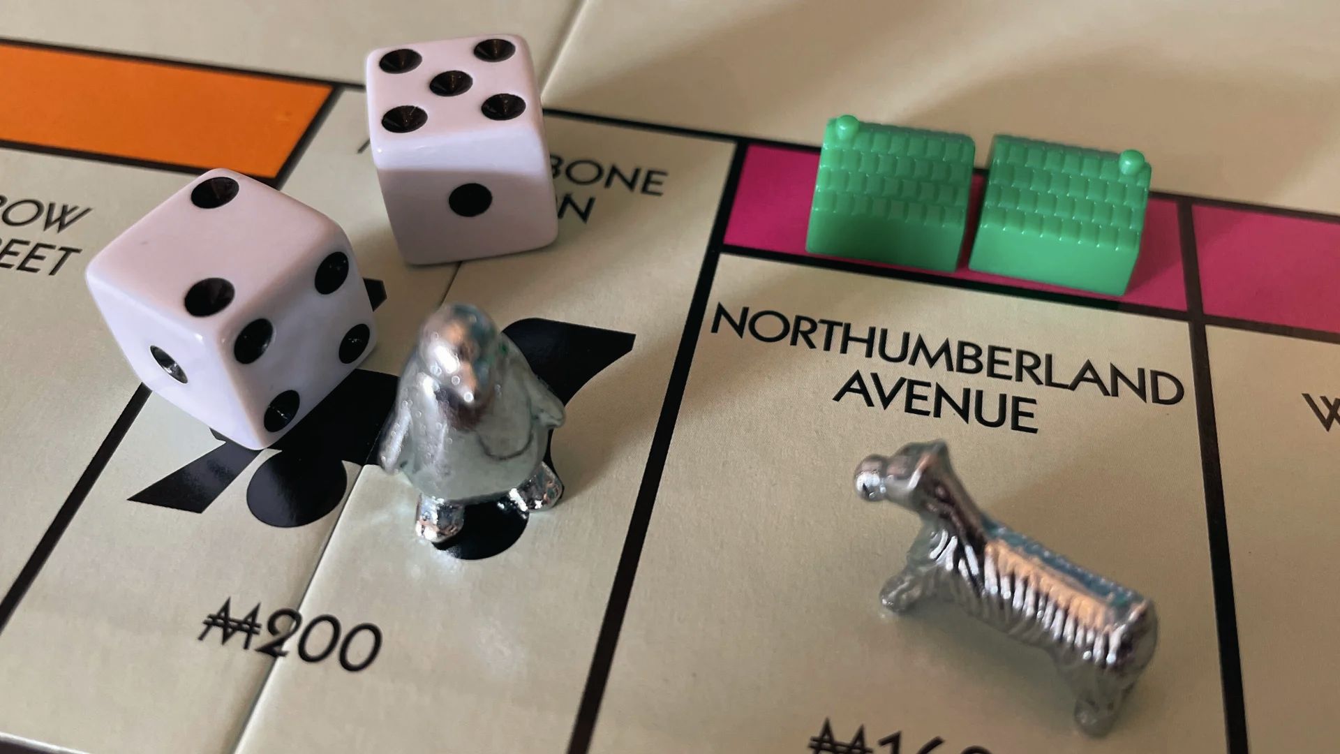 Close-up Monopoly board with dice, penguin and dog tokens on Northumberland Ave for mid levels.
