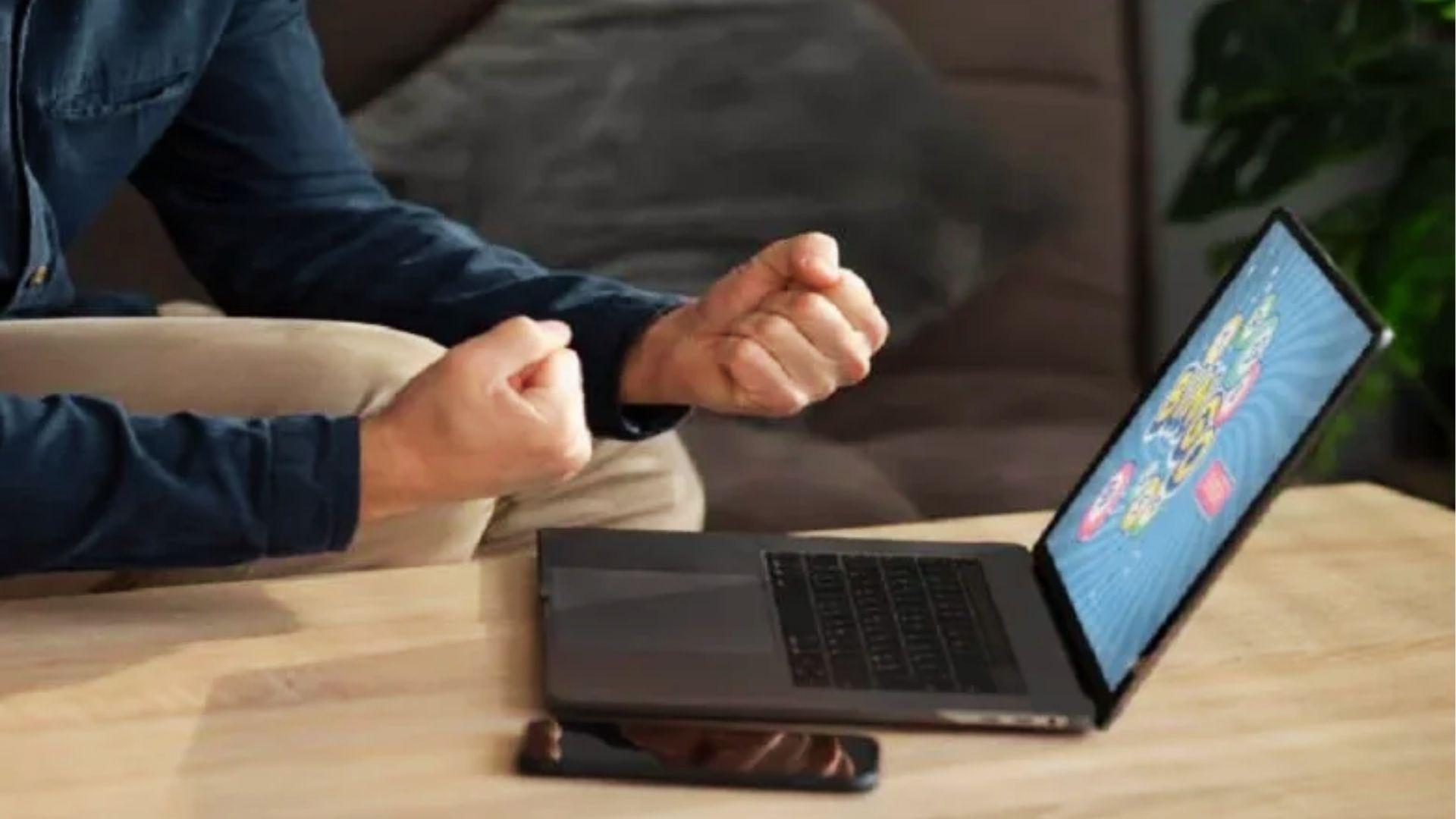 Gamer clenching fists in excitement while playing colorful game on laptop at home on PlayBattleSquare