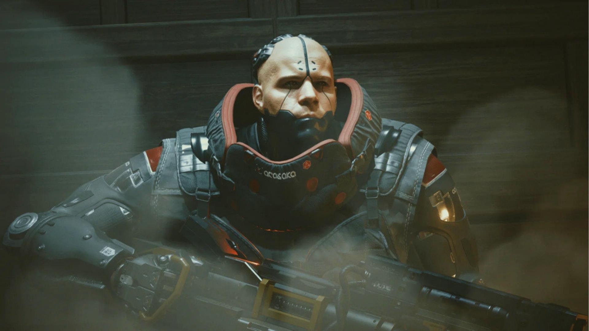 Adam Smasher, fully converted Arasaka cyborg with heavy combat armor and faceplate, grips rifle in smoke-filled battlefield environment.