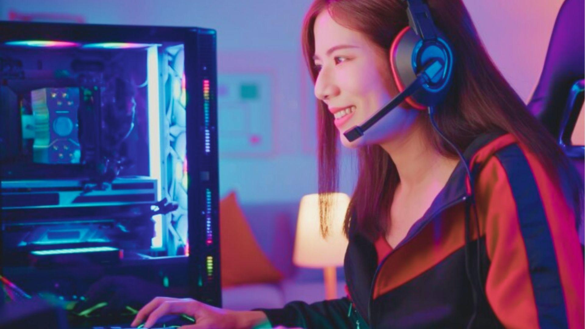 Female streamer smiles while gaming on a transparent PC case with rainbow LED fans.