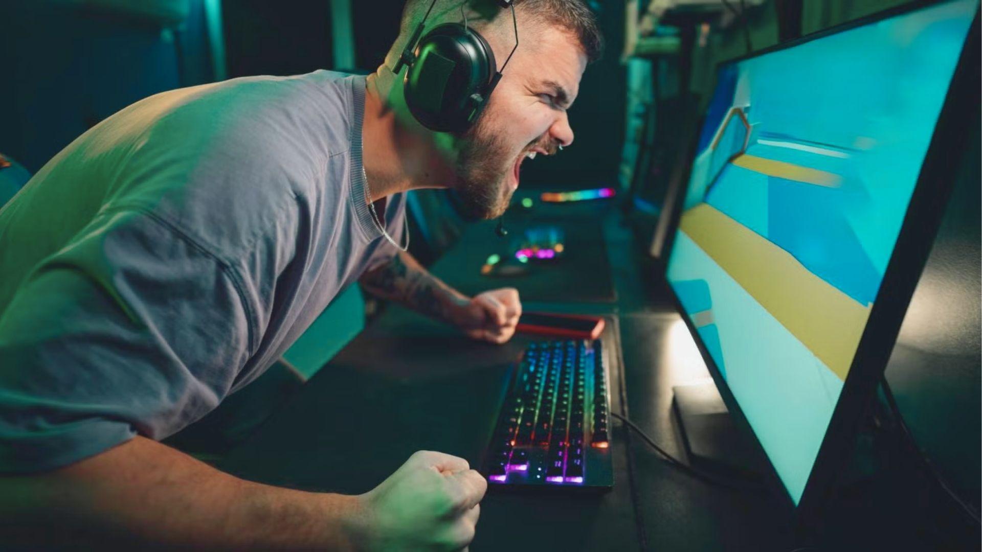 An intense PC gamer shouts at his screen with fists clenched during a competitive match.